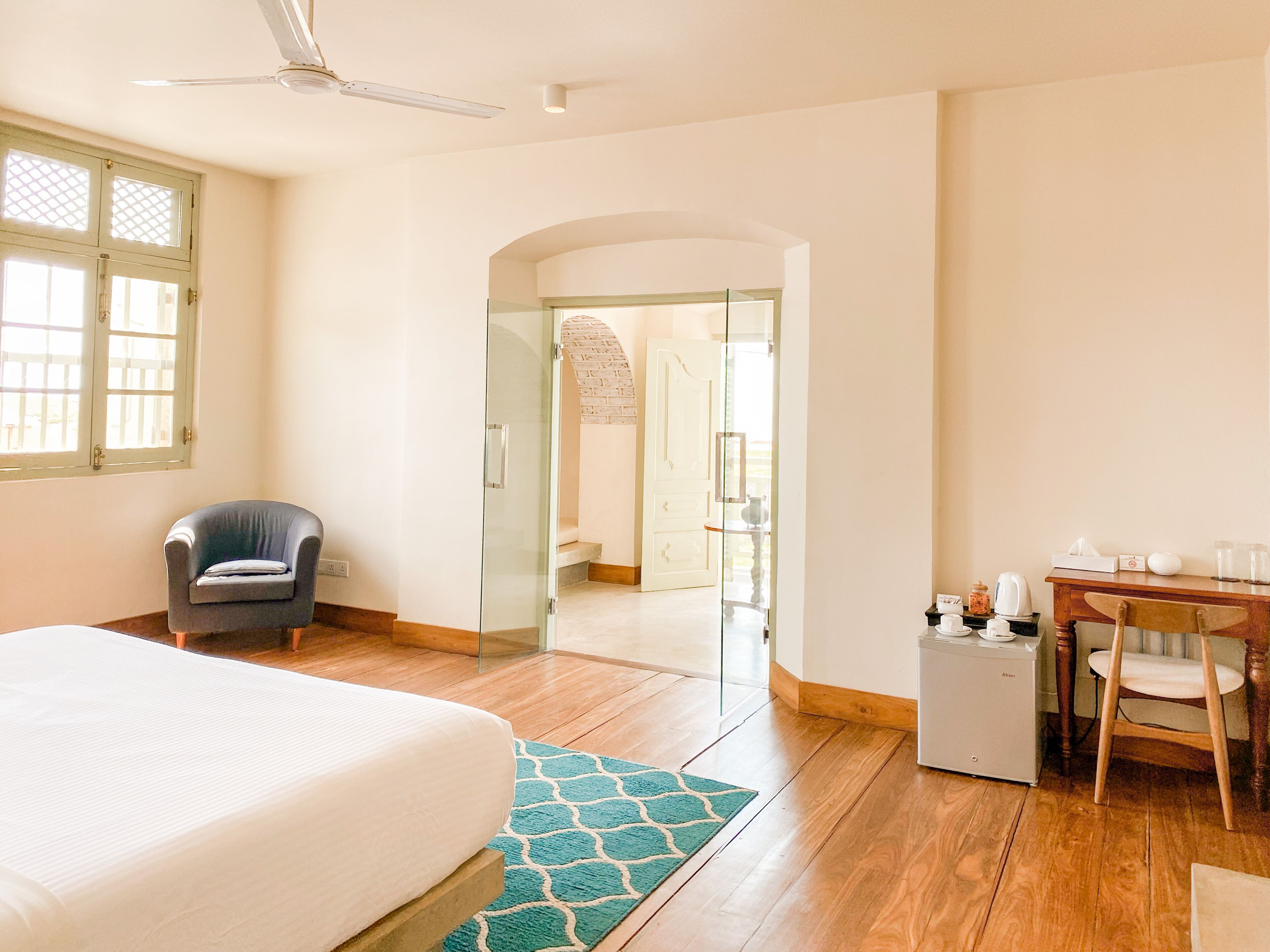 A hotel room with a bed, a desk, a chair, a small refrigerator, and a window.