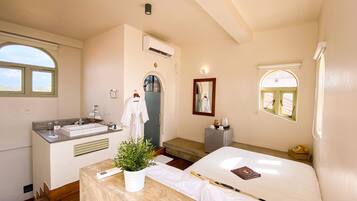 A hotel room with a bed, a bedside table with a plant, a bathroom with a sink and mirror, and a window with a view.