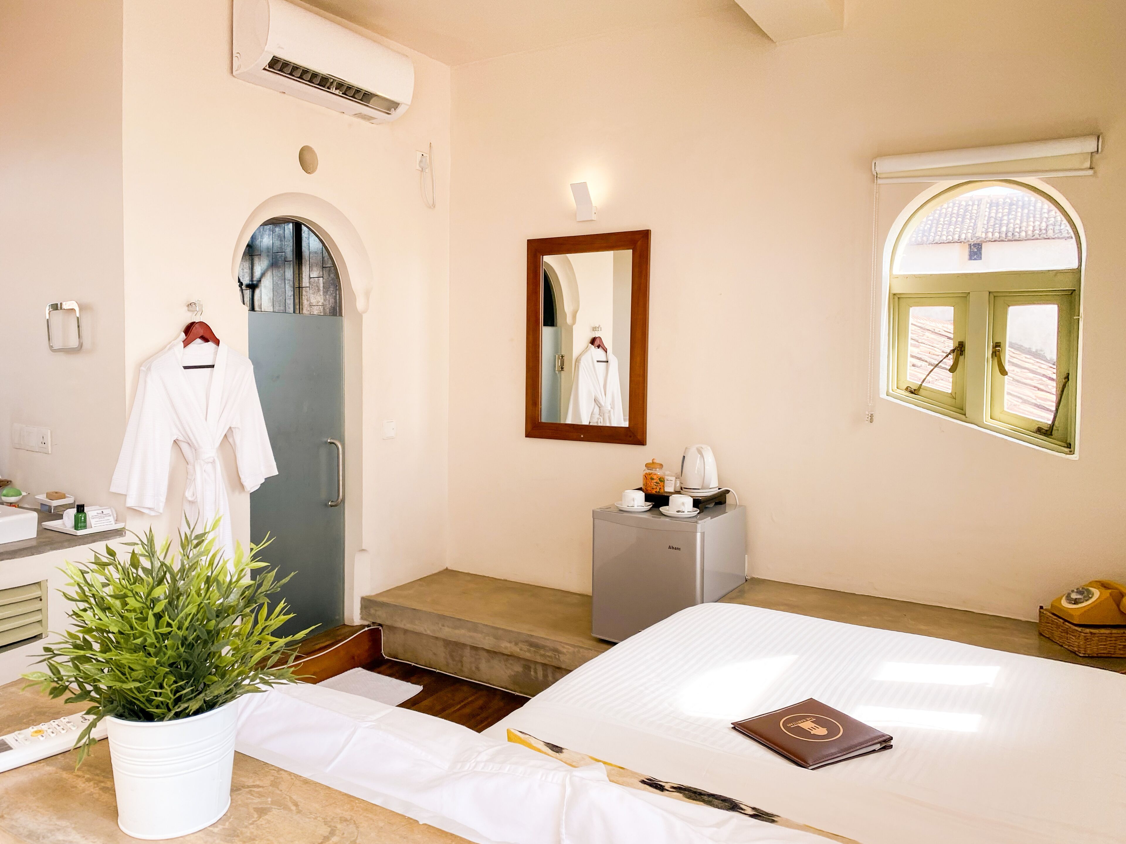 Habitación de hotel con cama, un escritorio pequeño, una planta en maceta, un espejo y ventana con vistas.