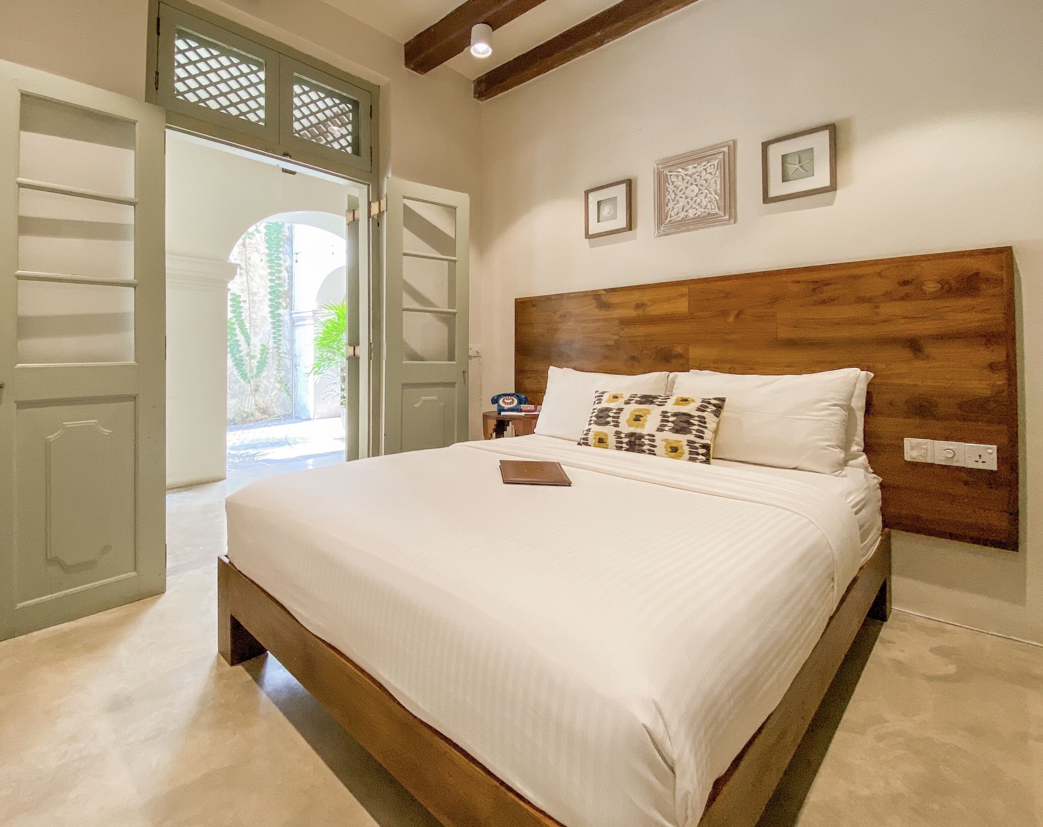 A bedroom with a wooden headboard, a bed with white linens, and a small bedside table with a lamp.