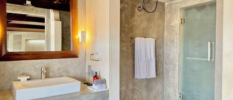 A bathroom with a white sink, a mirror, a towel rack, and a glass shower door.