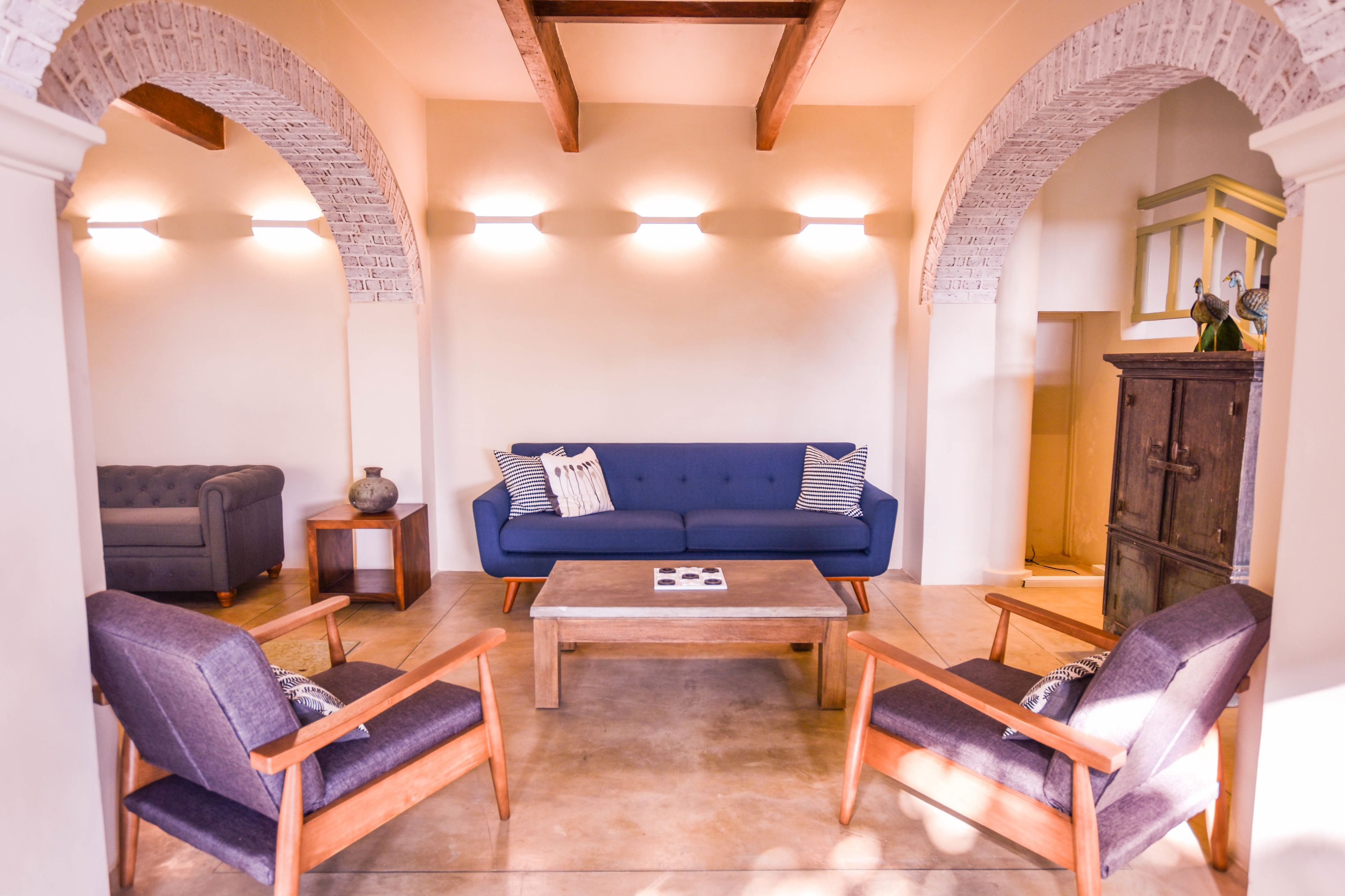A living room with a blue sofa, two wooden chairs, a coffee table, and a cabinet with decorative items.