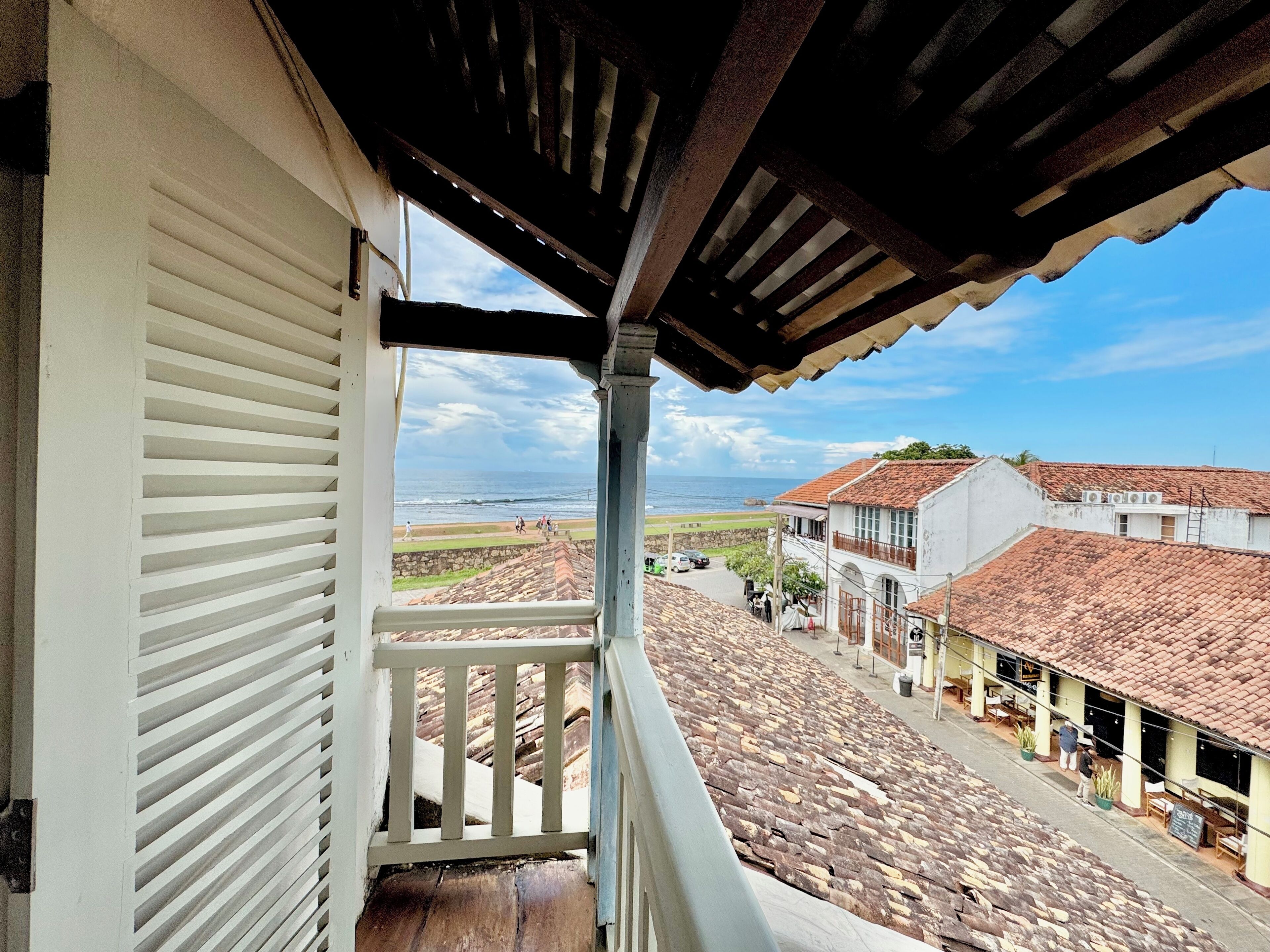 A balcony with a view of a coastal street and buildings with red-tiled roofs.