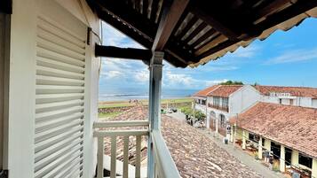 A balcony with a view of a coastal street and buildings with red-tiled roofs.