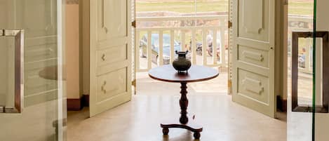 An open doorway leading to a balcony with a table and chairs, overlooking a coastal view.