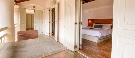 A hotel room with a wooden ceiling, a bed with a wooden headboard, and a bathroom with a shower and toilet visible through an open door.