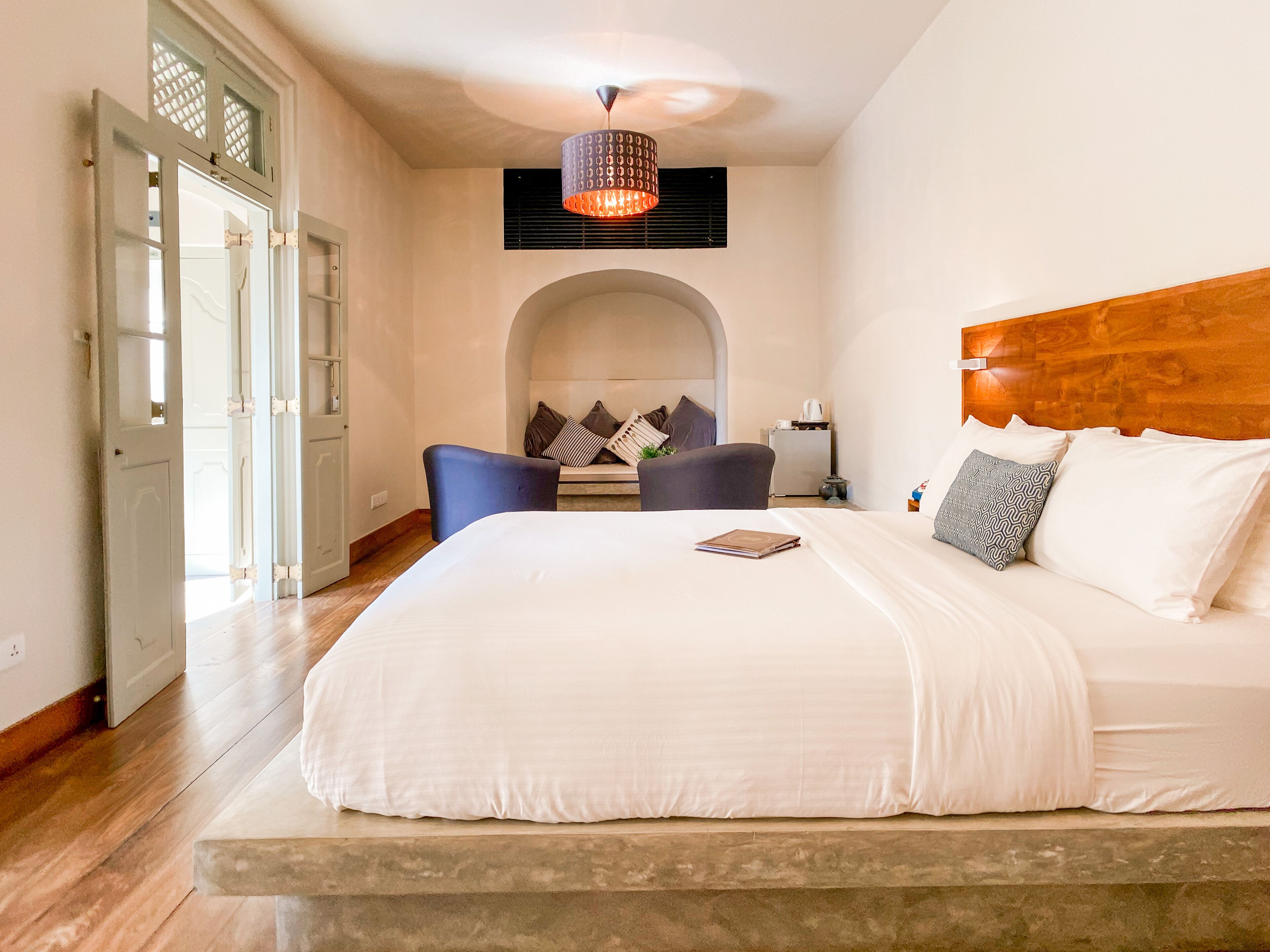 A bedroom with a large bed, a wooden headboard, a blue chair, and a small table with a lamp.