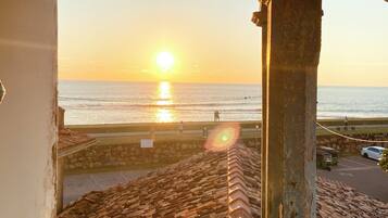 A balcony with a view of the sunset over the sea, a stone wall, and a parked car.