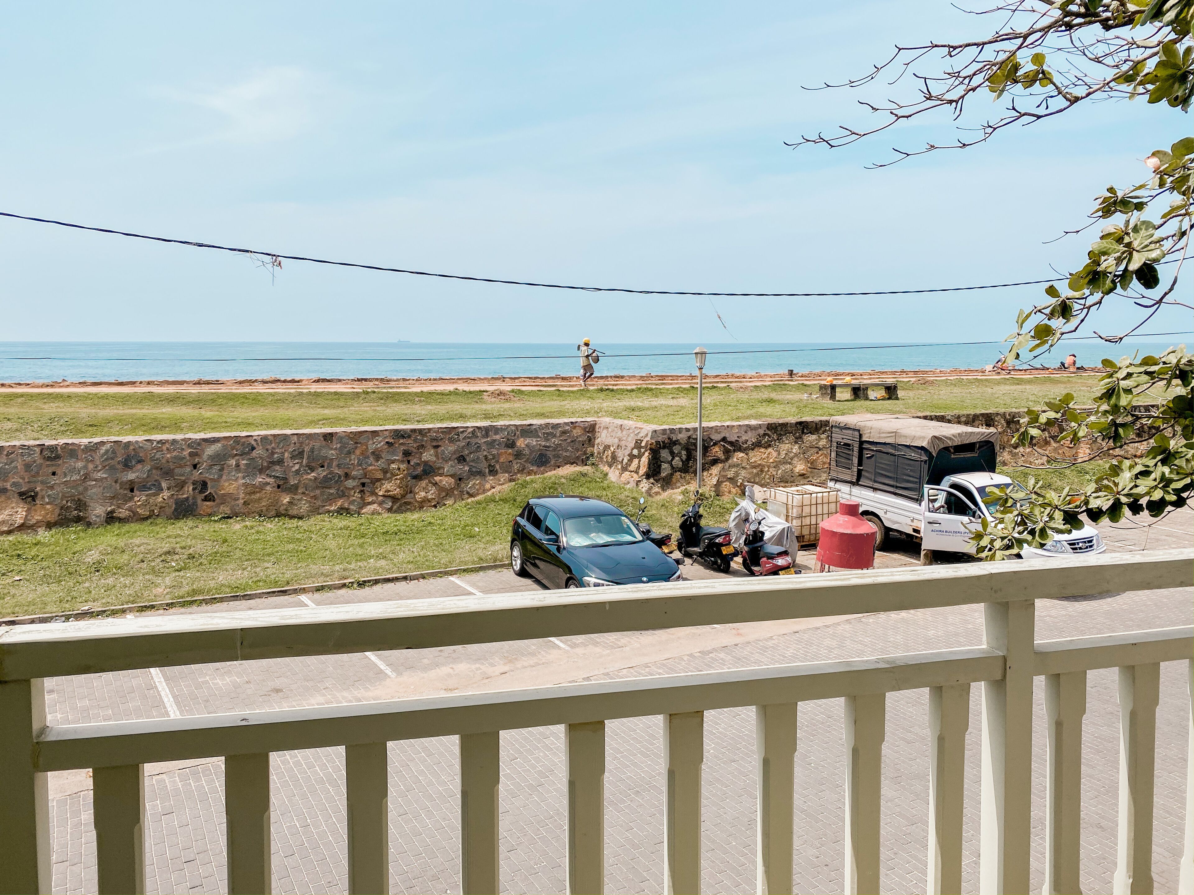 A coastal view with a stone wall, parked vehicles, and a clear sky.