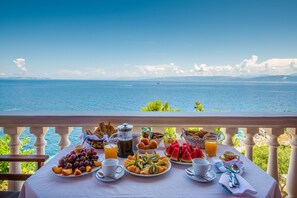A breakfast table with fruits, pastries, and beverages, overlooking a scenic ocean view. - Paxos Sunrise Villas (Paxos)