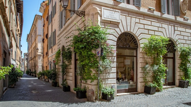 A narrow cobblestone street lined with historic buildings, featuring a shop with a large arched window and signage. - The Right Place 4U Roma Navona Terrace Luxury Rooms (Rome)
