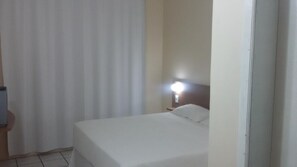 Quarto de hotel com uma cama, mesa de cabeceira com abajur e cortina.