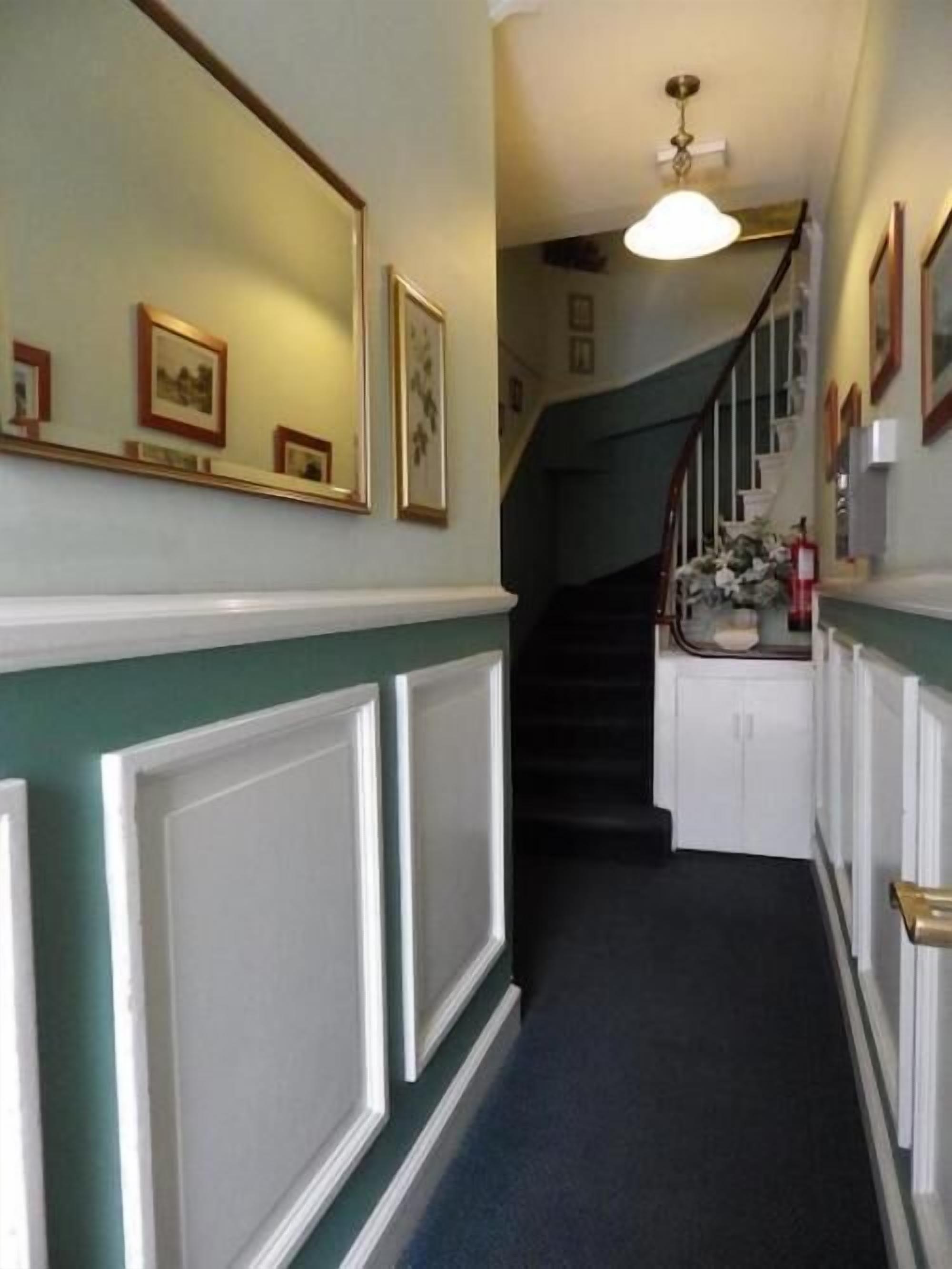 A hallway with a staircase, framed pictures on the walls, and a light fixture above the stairs.