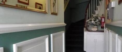 A hallway with a staircase, framed pictures on the walls, and a light fixture above the stairs.