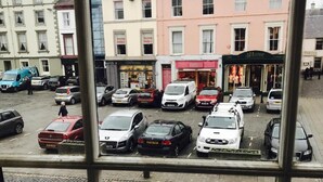 Straßenansicht mit parkenden Autos, einem Gebäude mit Schildern für häusliche Hilfe und einem Geschäft namens 'A Hume'.