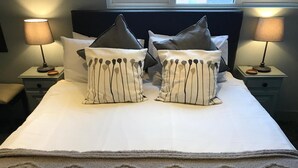 Ein ordentlich gemachtes Bett mit gestreifter Bettwäsche, einer passenden Tagesdecke und je einer Nachttischlampe auf den Nachttischen.
