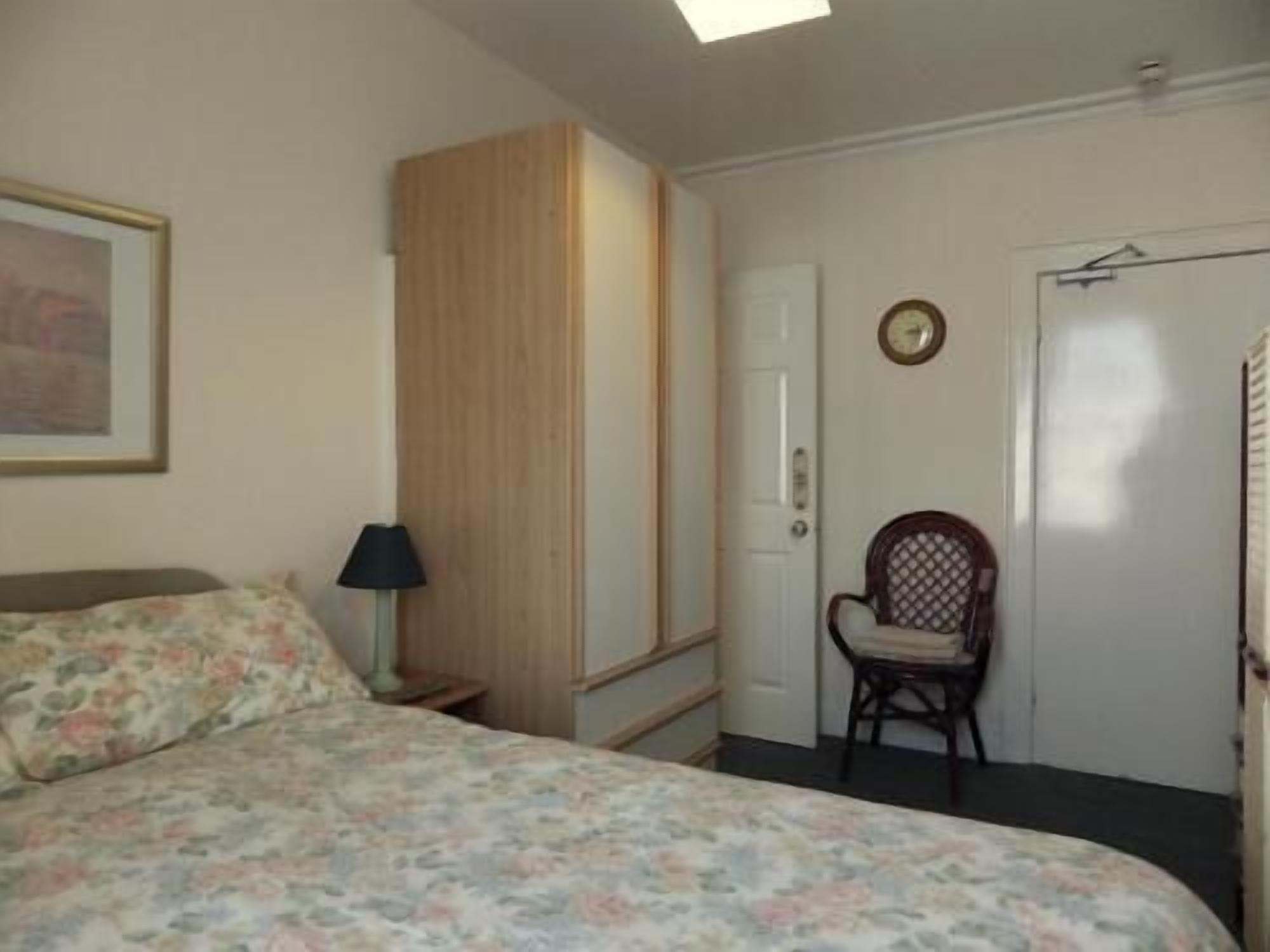 Un dormitorio con cama, una silla, un armario, una lámpara y un reloj en la pared.