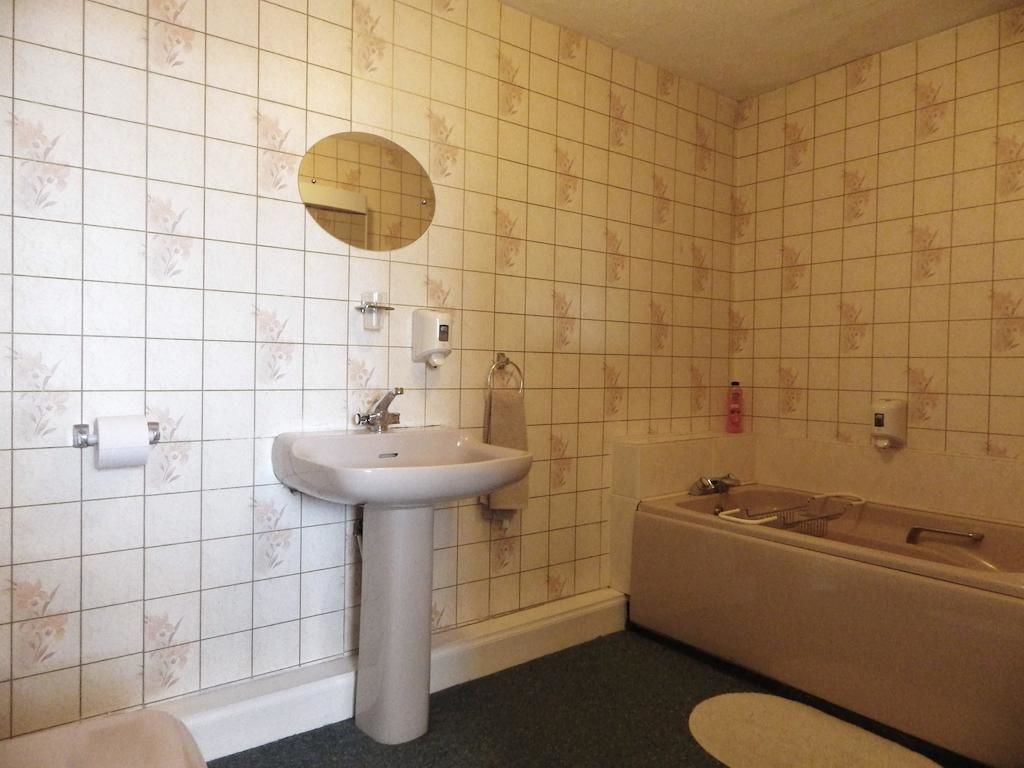 Un baño con lavamanos, espejo, papel higiénico y bañera.