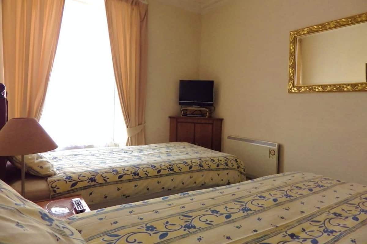 A hotel room with two beds, a television on a small table, a lamp, and a large mirror on the wall.