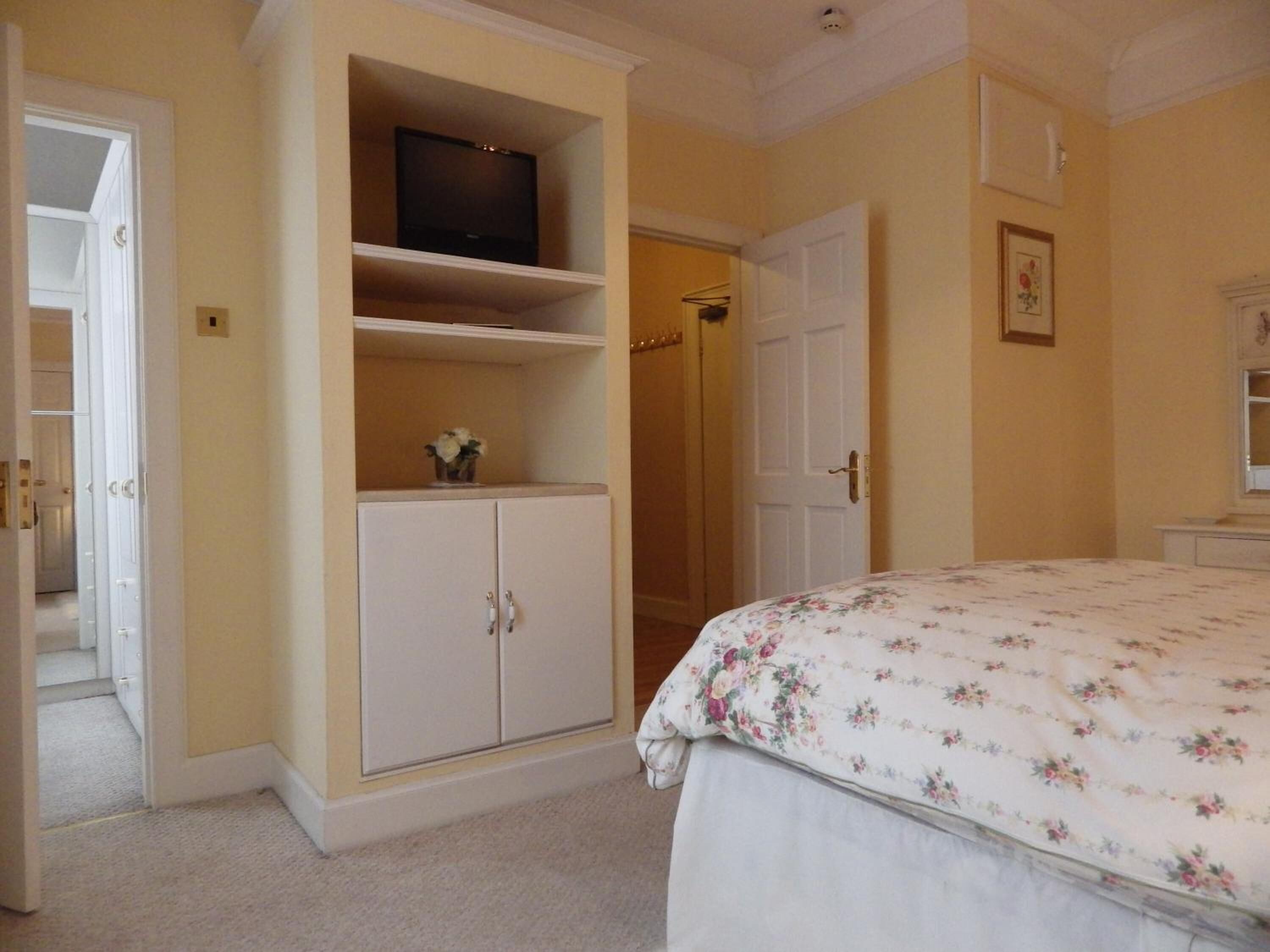 A bedroom with a bed, a wardrobe, a television on a shelf, and a door leading to another room.