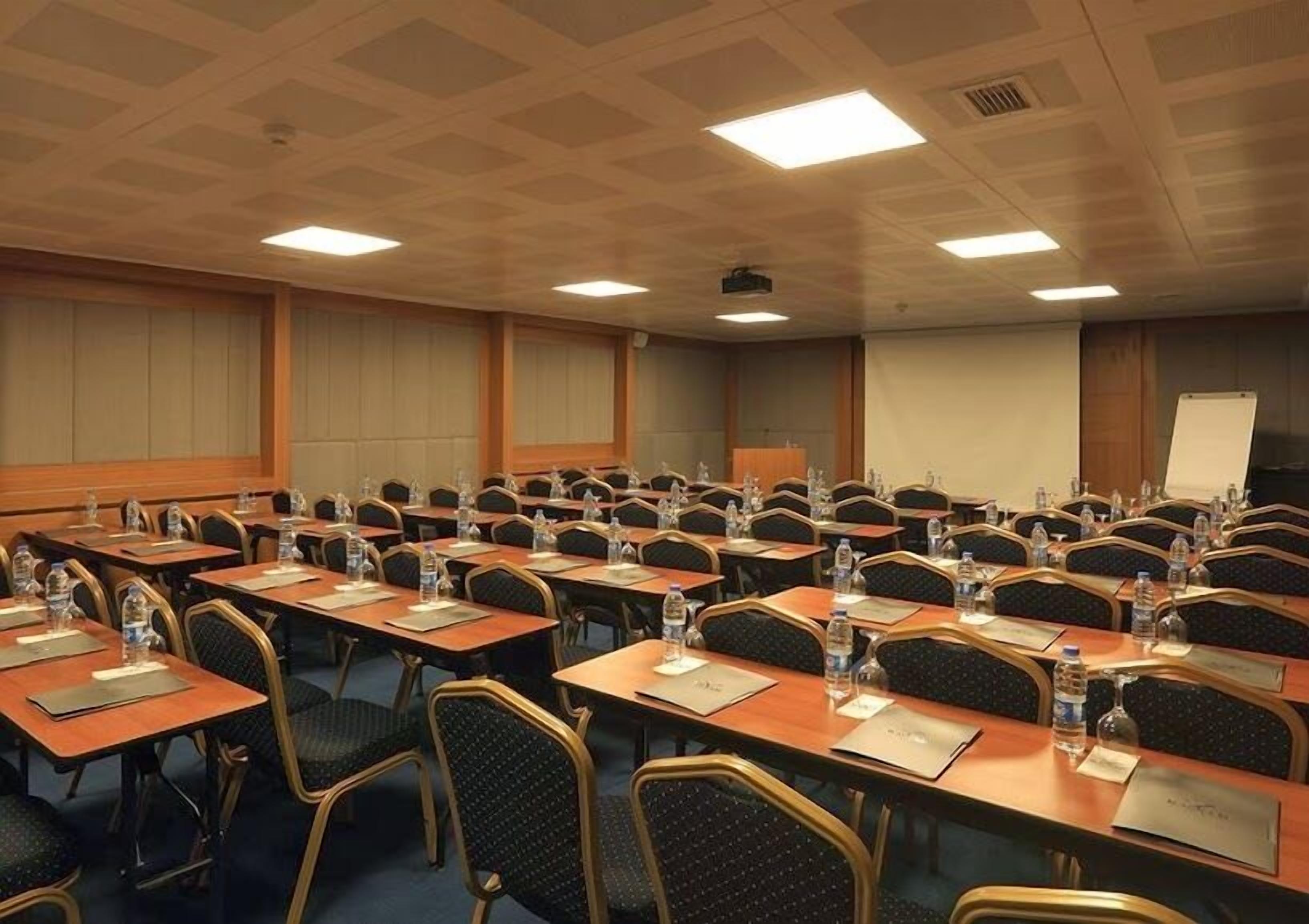 A conference room with rows of tables and chairs, equipped with water bottles and nameplates, and a whiteboard on the wall.