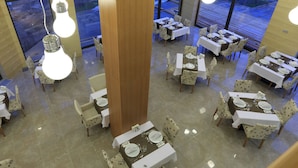 A restaurant with multiple tables and chairs, each set with white tablecloths and neatly arranged table settings. - Kaçkar Resort Hotel (Camlihemsin)
