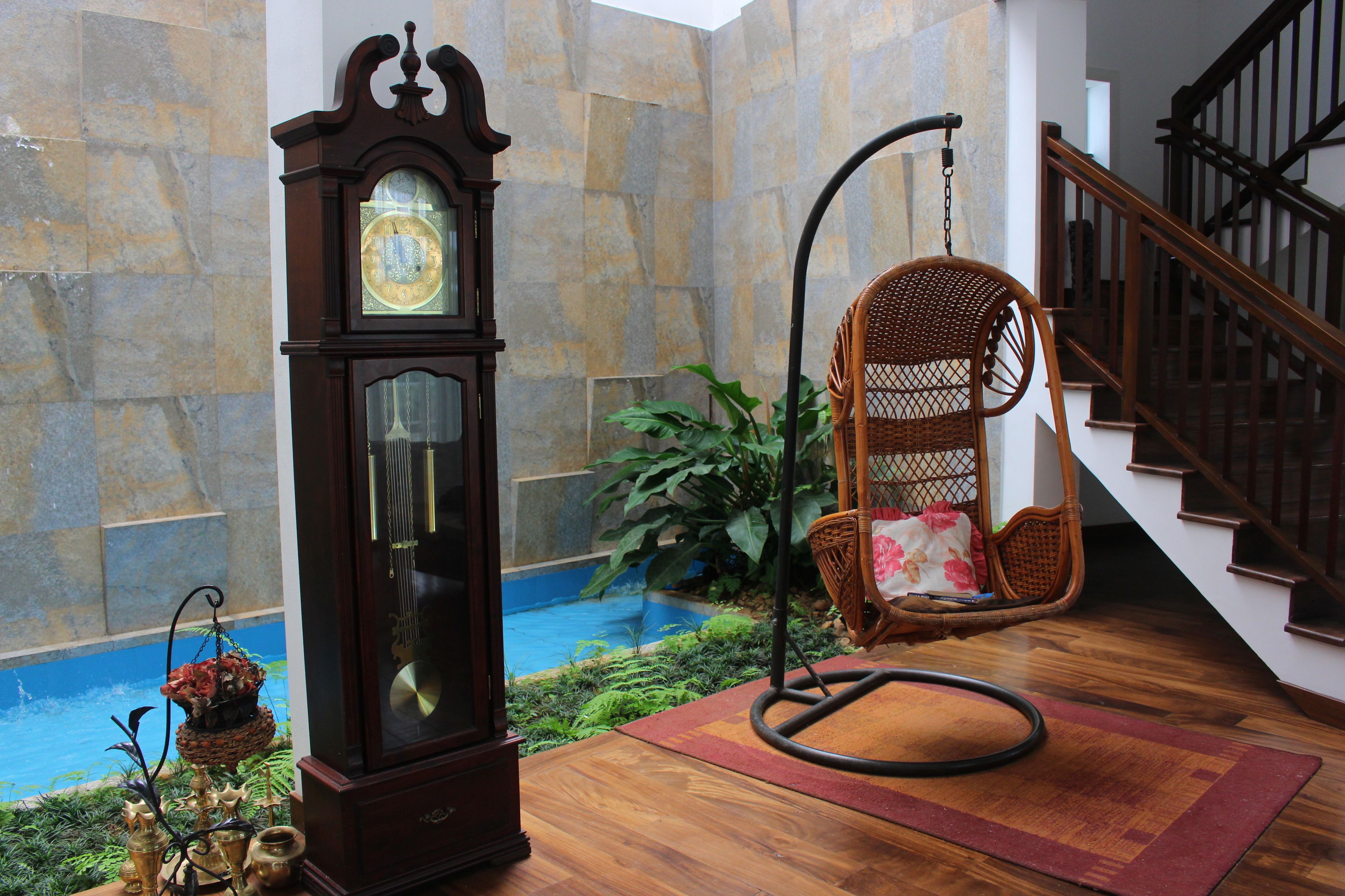 Une pièce avec une grande horloge comtoise, un fauteuil suspendu et un escalier.