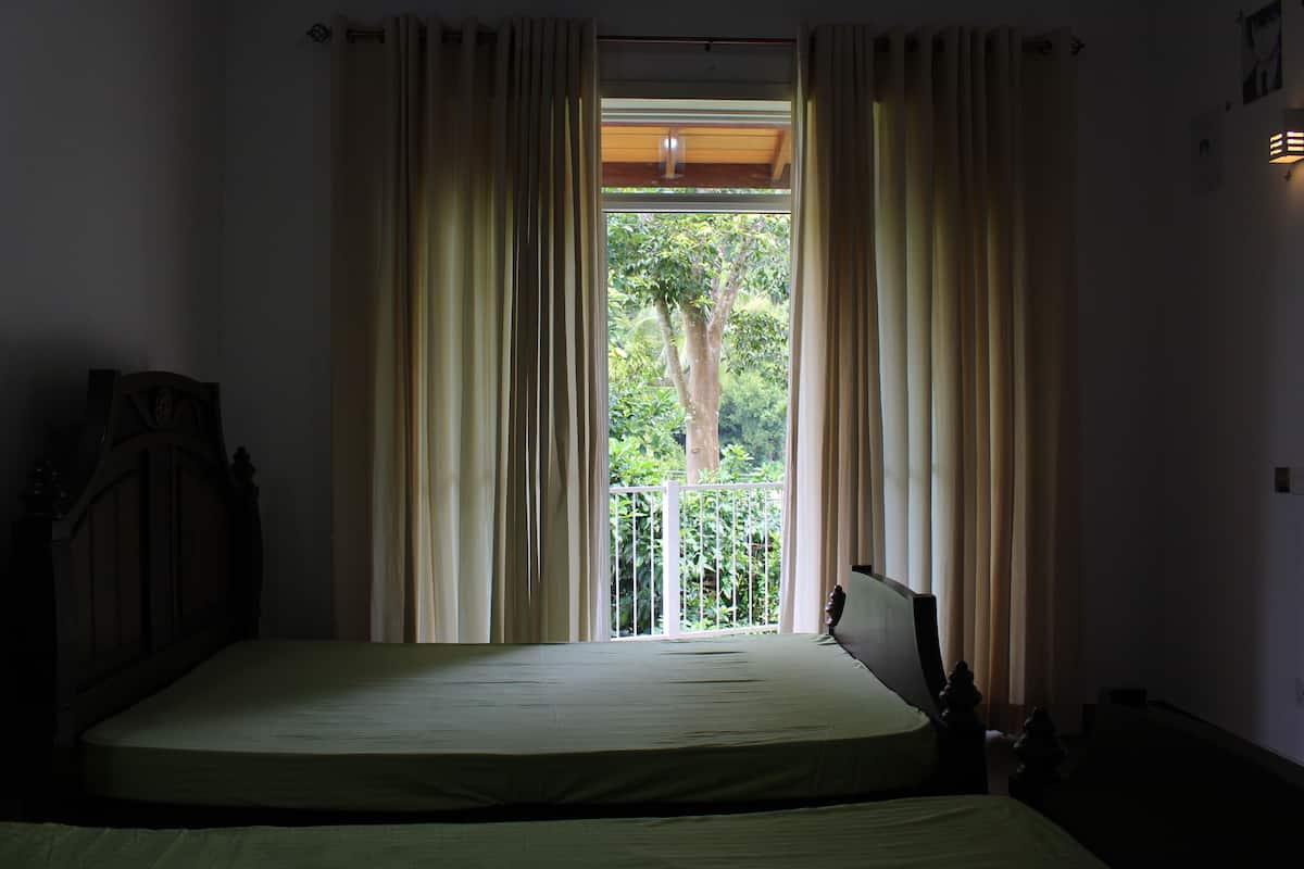 A bedroom with a bed, a wooden headboard, and a view of greenery through a window with curtains.