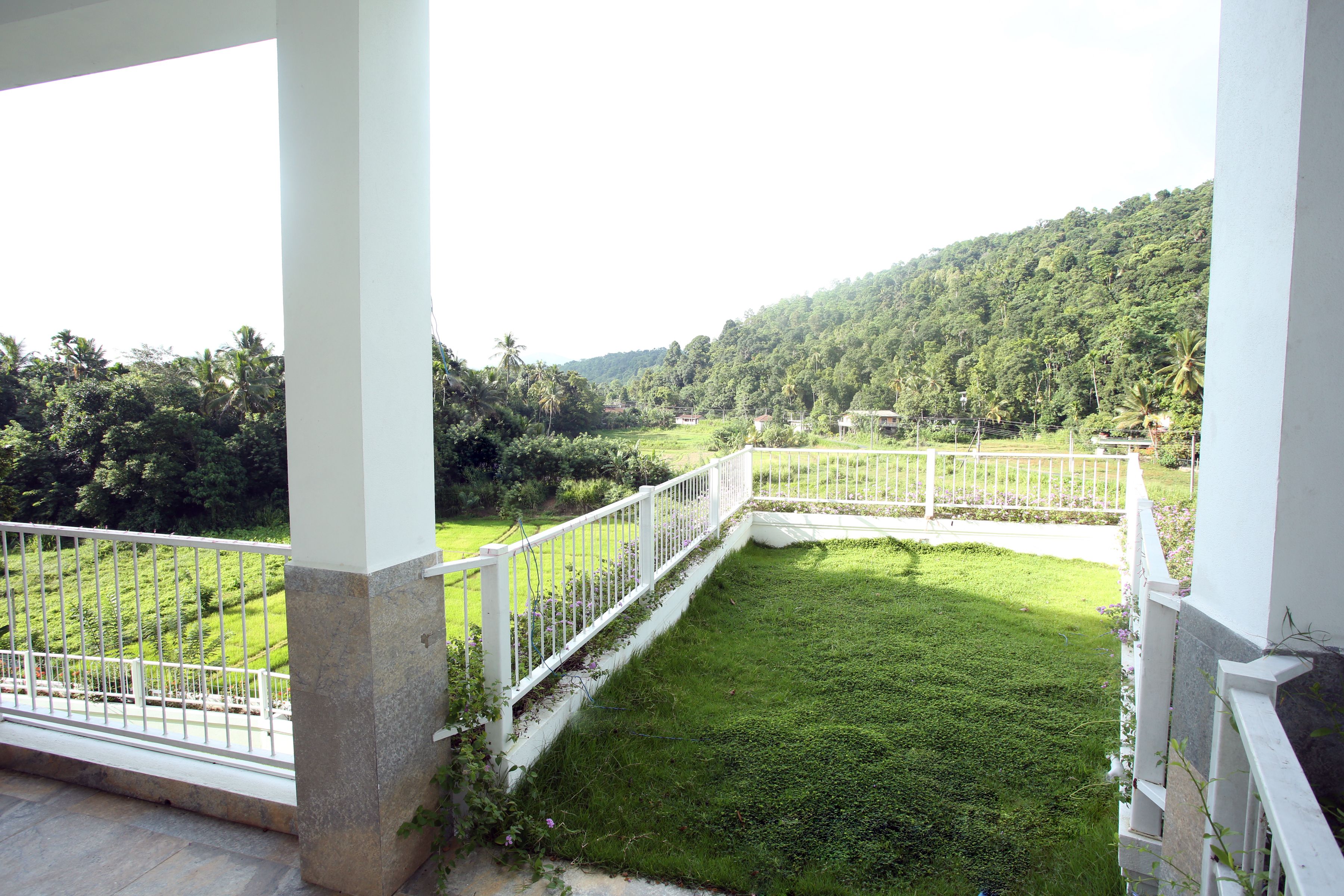 A balcony with white railings overlooking a lush green lawn and a hilly landscape.