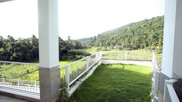 A balcony with white railings overlooking a lush green lawn and a hilly landscape.