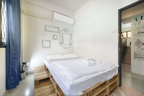 A room with a bed on a wooden pallet, white bedding, a desk with a lamp, and a window with blue curtains. - Sloth Hostel (Bangkok)