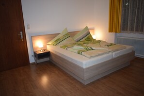Een slaapkamer met een bed, nachtkastje, lamp en een raam met gordijnen.