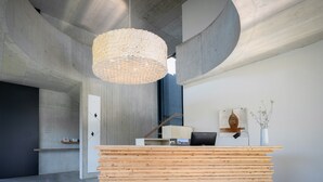 A reception desk with a wooden slat design, a hanging woven light fixture, and a wall-mounted artwork.