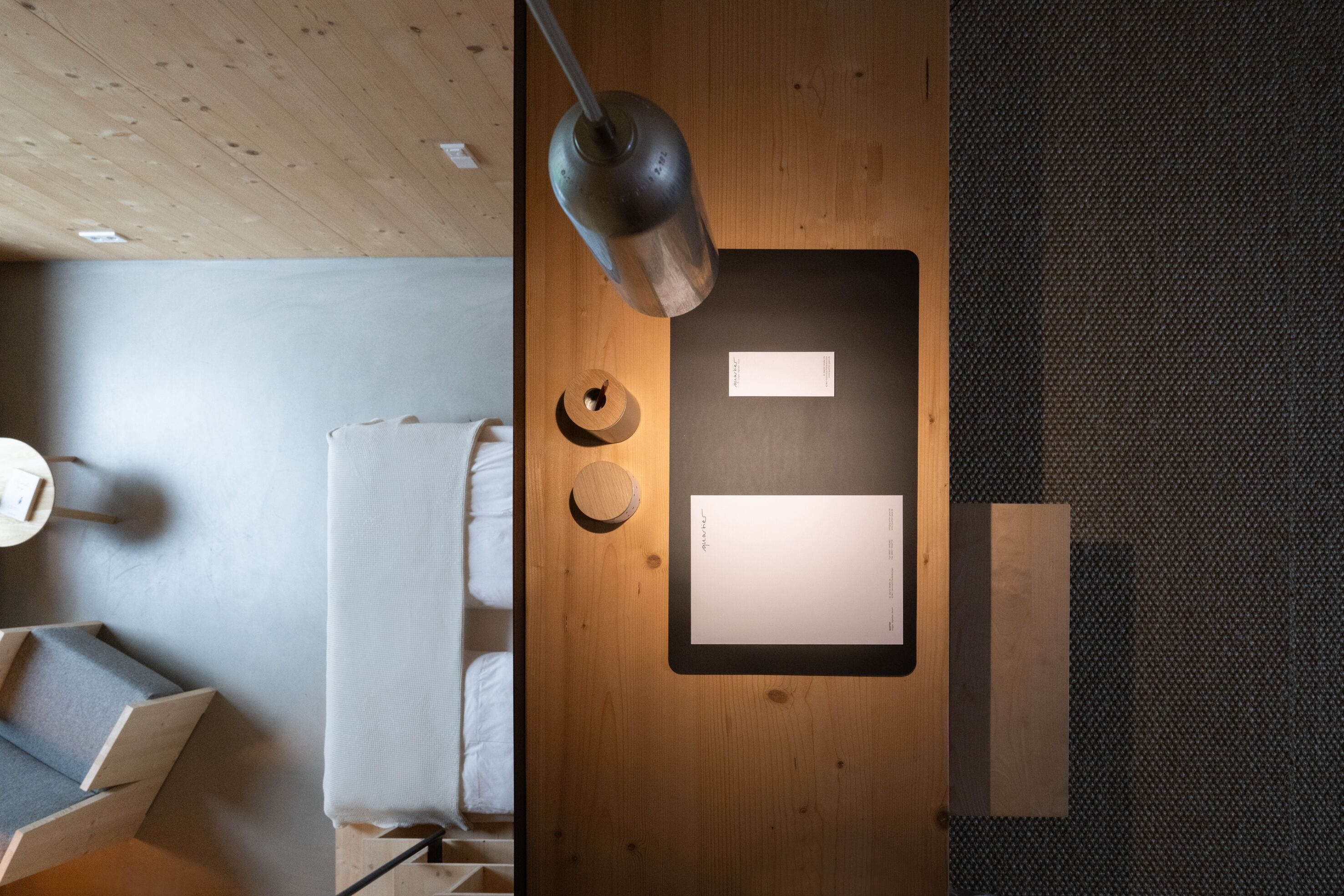A modern room with a wooden ceiling, a bed with white bedding, a desk with a lamp, and a small round table.
