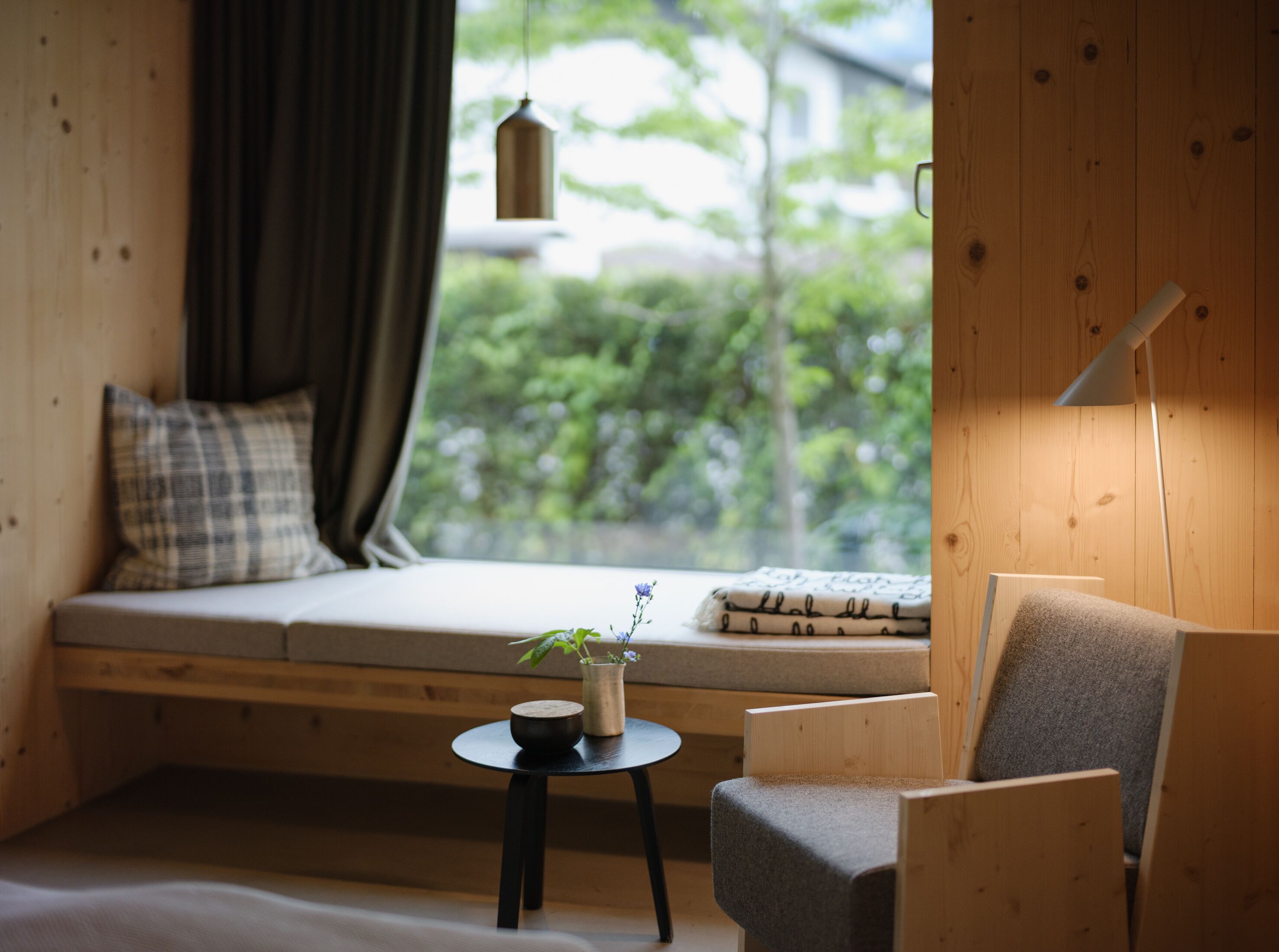 A cozy room with a wooden floor, a sofa with a cushion, a small table with a bowl and a plant, and a lamp.