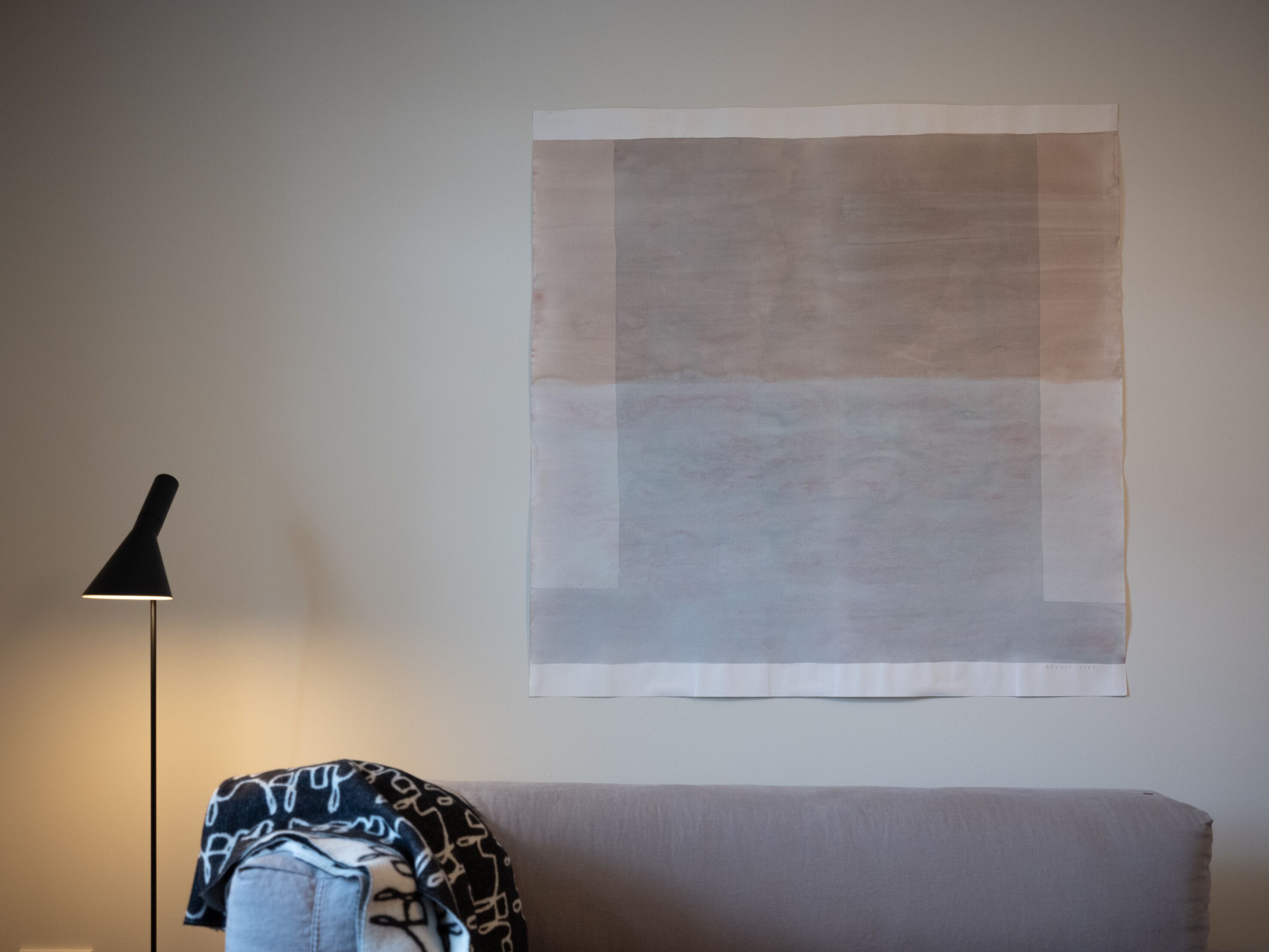 Una habitación con una obra de arte abstracta de gran tamaño en la pared, una lámpara de pie y un sofá con una manta estampada.