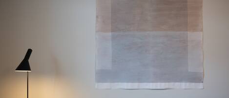 Una habitación con una obra de arte abstracta de gran tamaño en la pared, una lámpara de pie y un sofá con una manta estampada.
