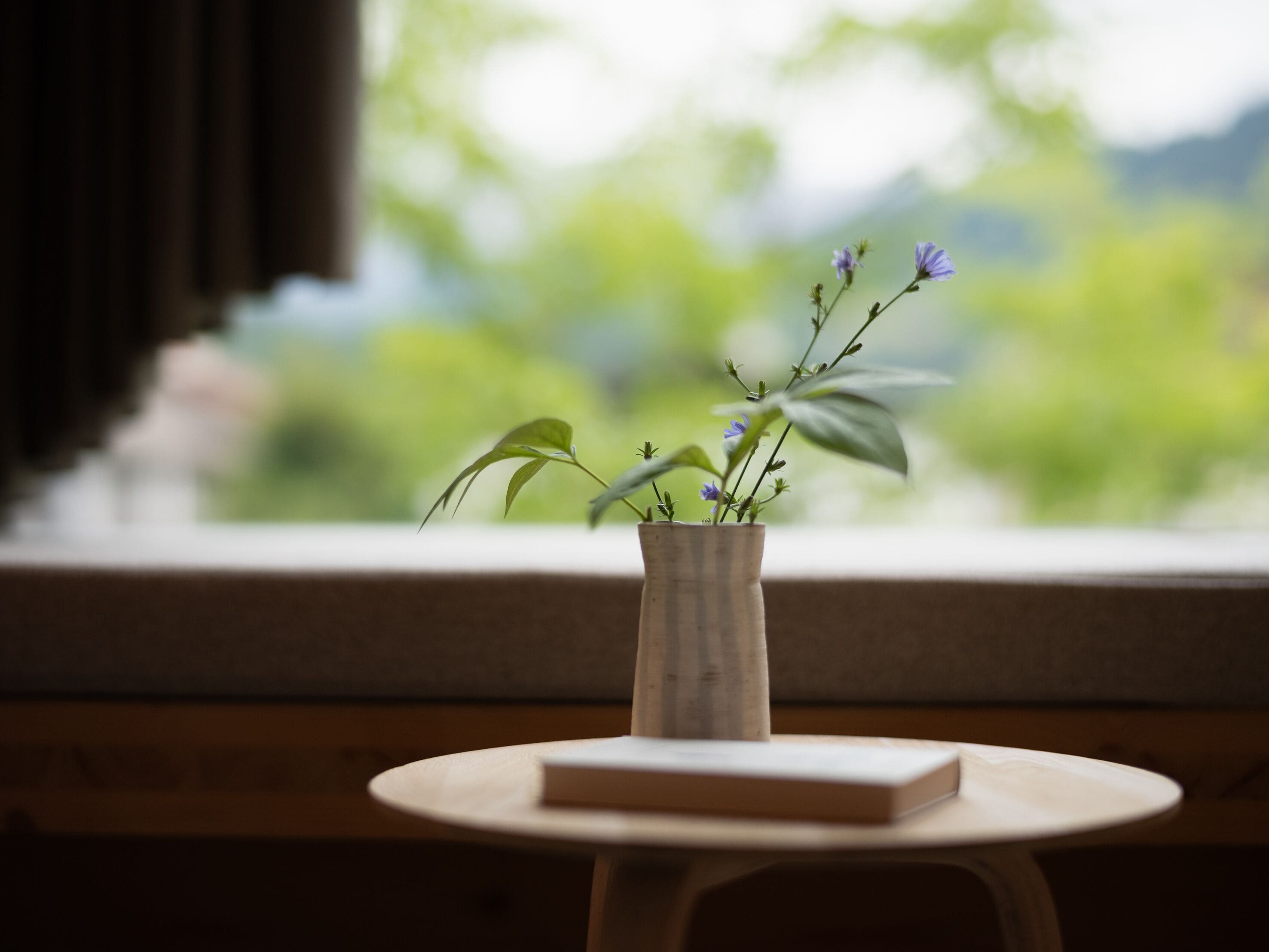 Ett litet runt bord med en vas som innehåller blommor och en bok.