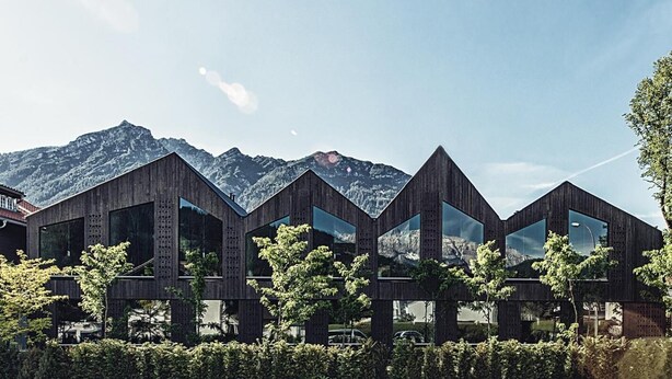 A modern building with a wooden exterior and large windows, set against a mountainous backdrop.