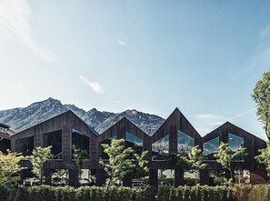A modern building with a wooden exterior and large windows, set against a mountainous backdrop. - quartier - Lodges Tagesbar Forum (Garmisch-Partenkirchen)