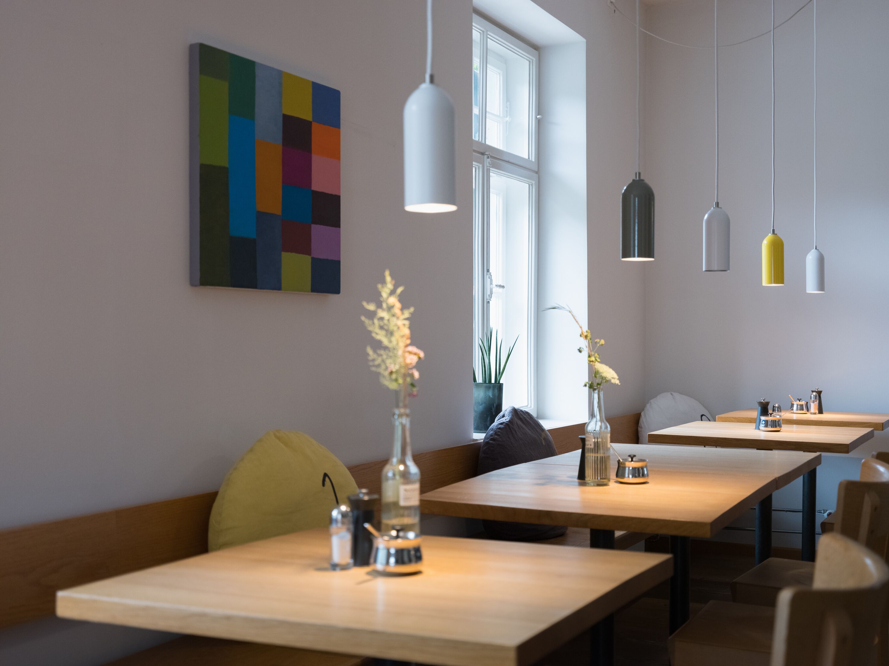 A modern dining area with wooden tables, benches, and hanging pendant lights.