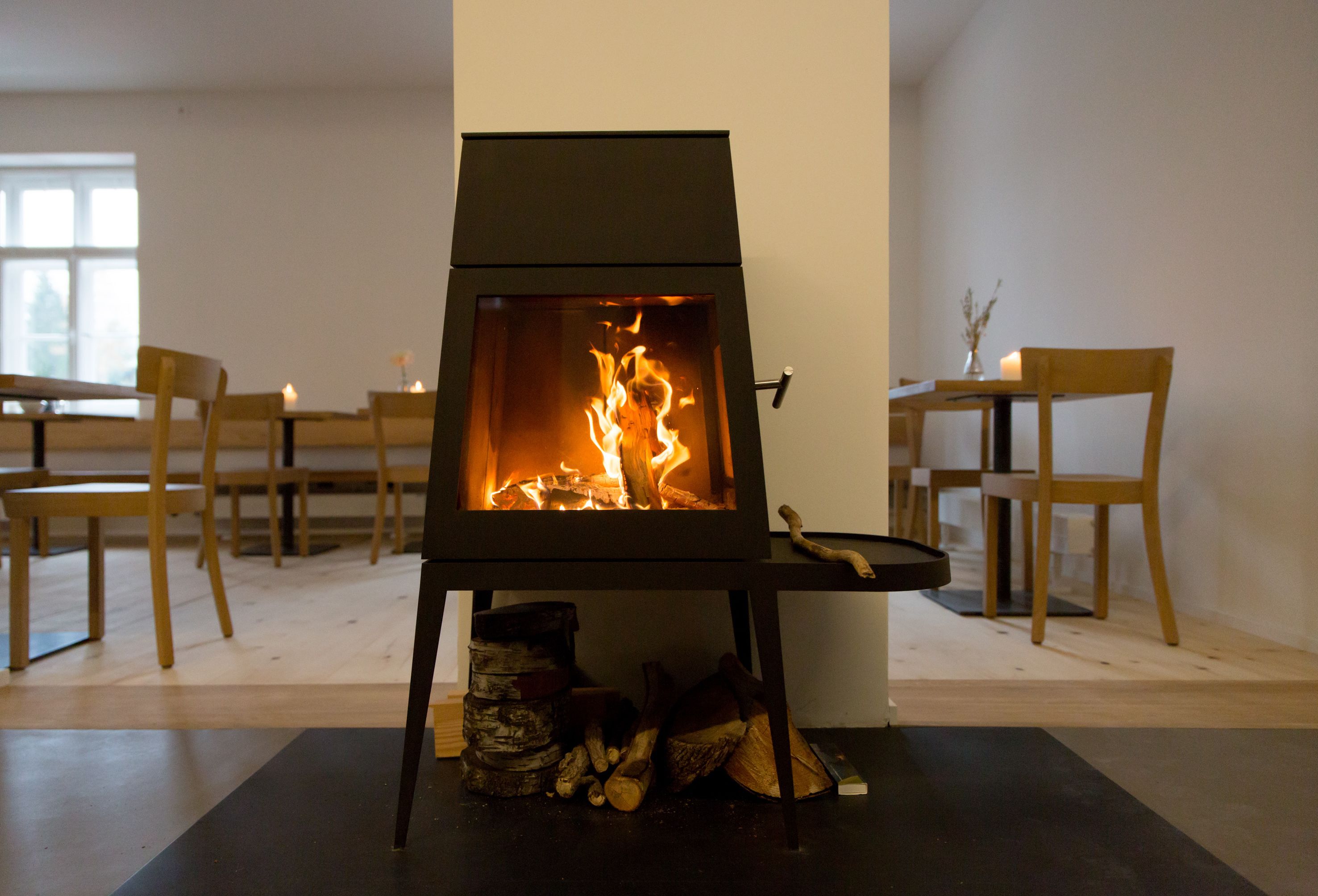 Ein moderner Kamin mit sichtbaren Flammen, umgeben von Holzmöbeln und einem Fenster im Hintergrund.