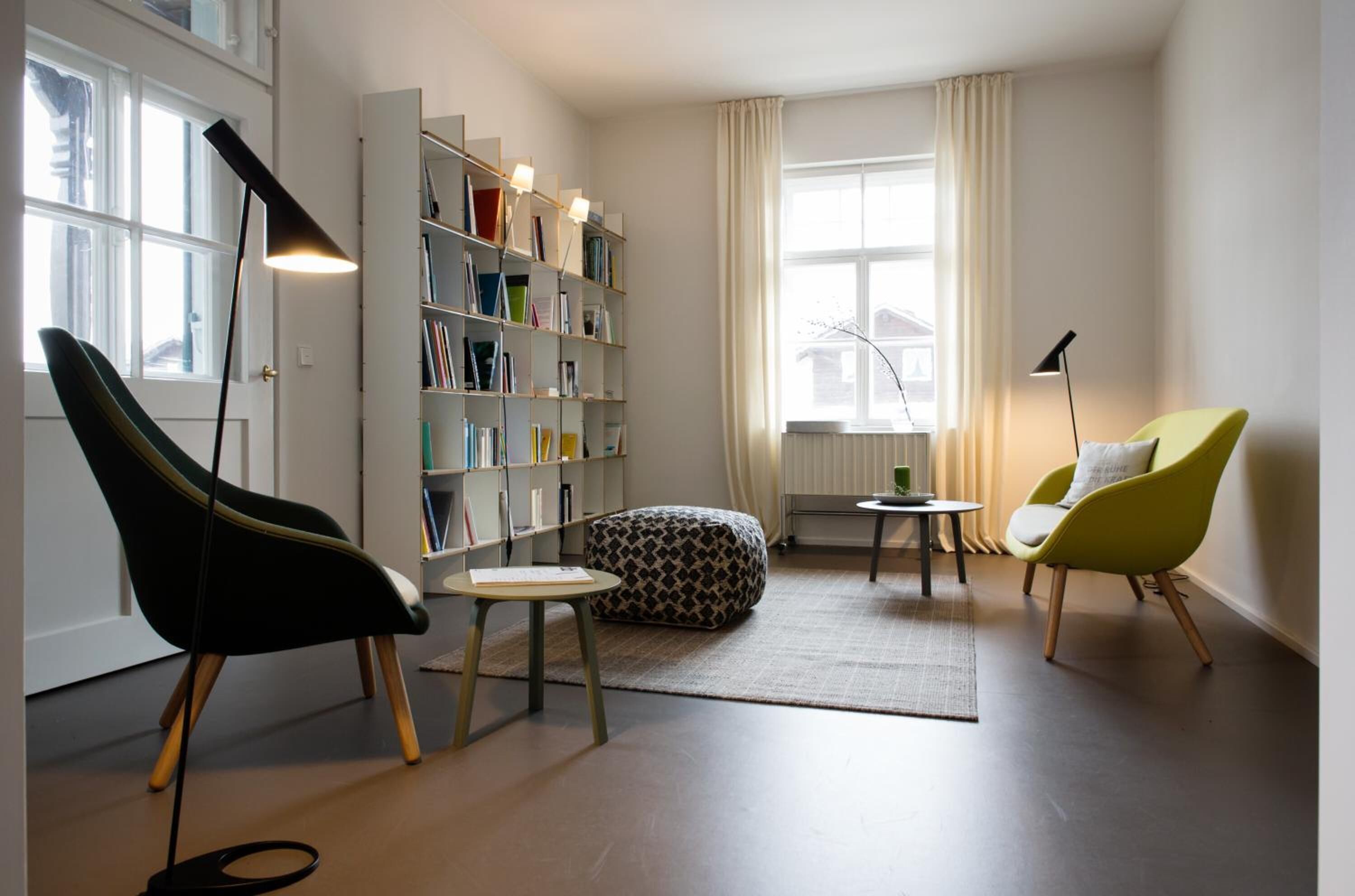 A modern living room with a bookshelf, two chairs, a round table, and a floor lamp.