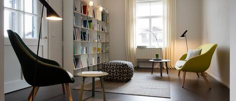 A modern living room with a bookshelf, two chairs, a round table, and a floor lamp.