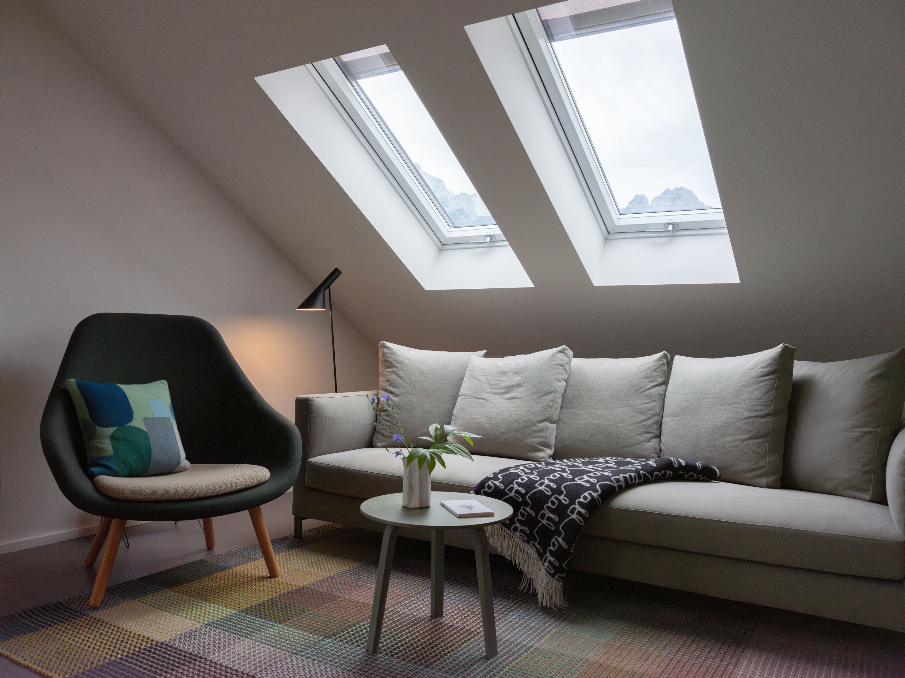 A modern living room with a high ceiling, two skylights, a sofa, a chair, a small table, and a floor lamp.