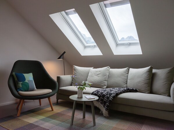 A modern living room with a high ceiling, two skylights, a sofa, a chair, a small table, and a floor lamp. - quartier - Lodges Tagesbar Forum (Garmisch-Partenkirchen)