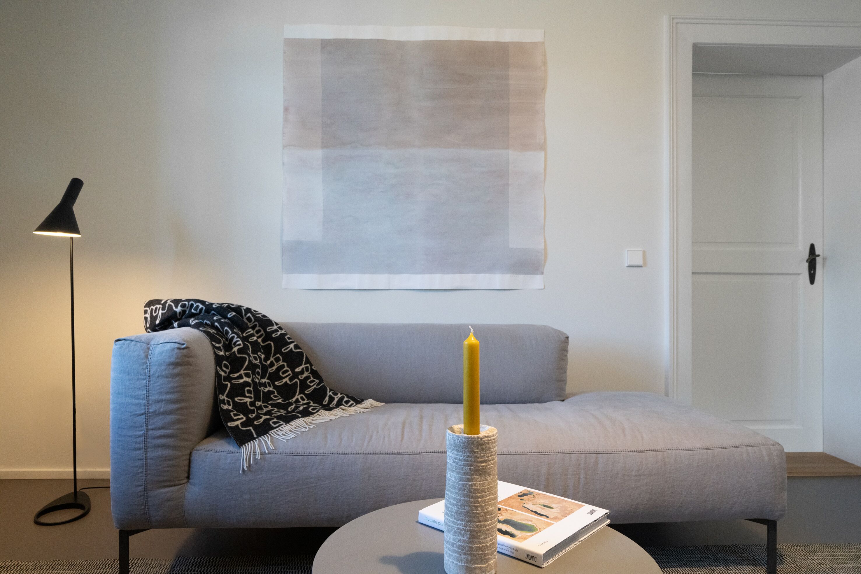 A modern living room with a grey sofa, a round coffee table, a floor lamp, and a large abstract painting on the wall.