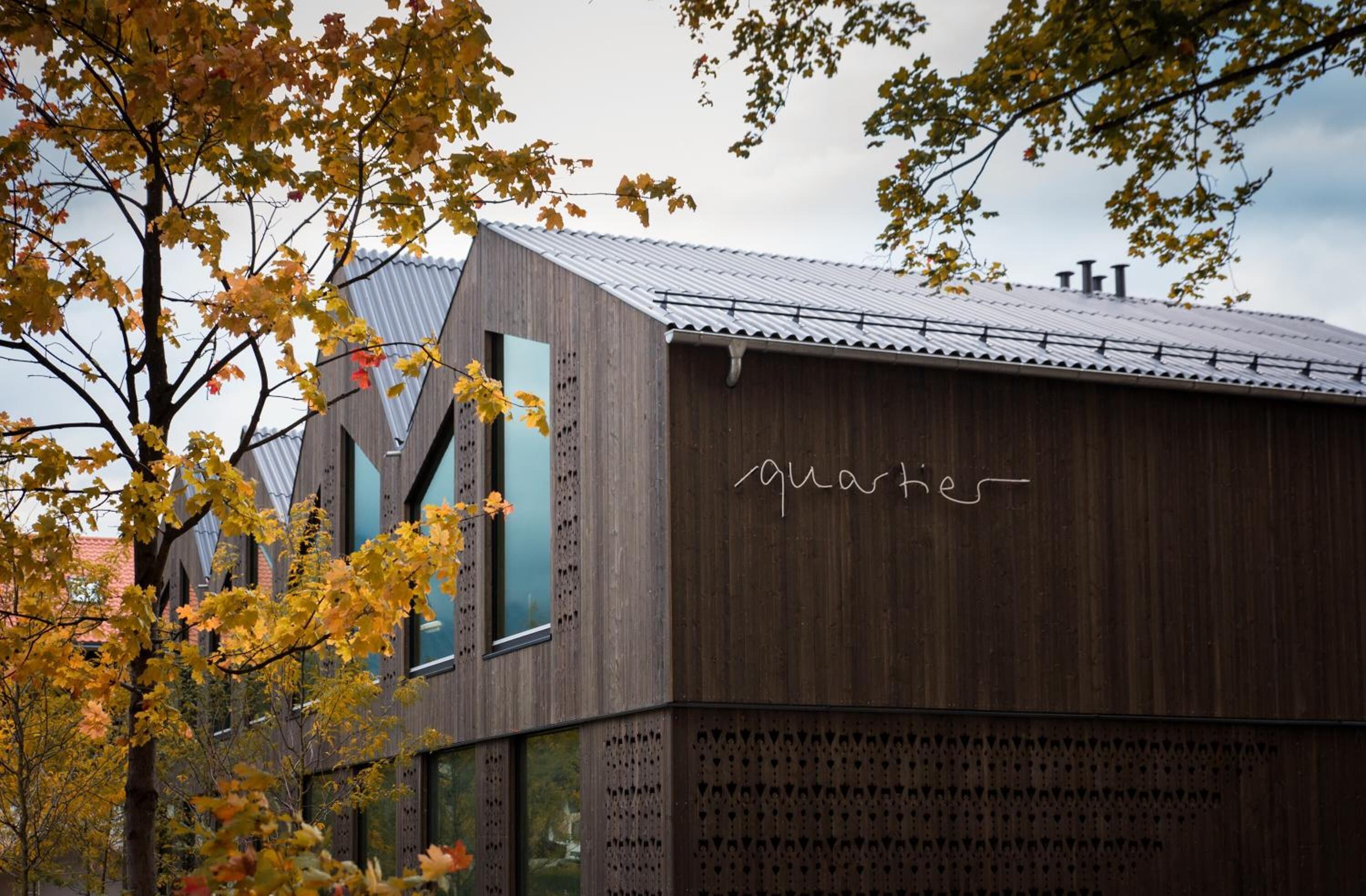 En moderne bygning med træfacade og metal tag, med teksten "quartier".