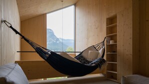 A hammock chair in a room with wooden walls and a large window overlooking mountains.