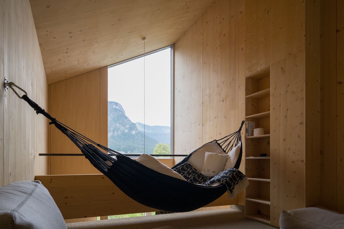 Ein Hängestuhl in einem Raum mit Holzwänden und einem großen Fenster mit Blick auf Berge.